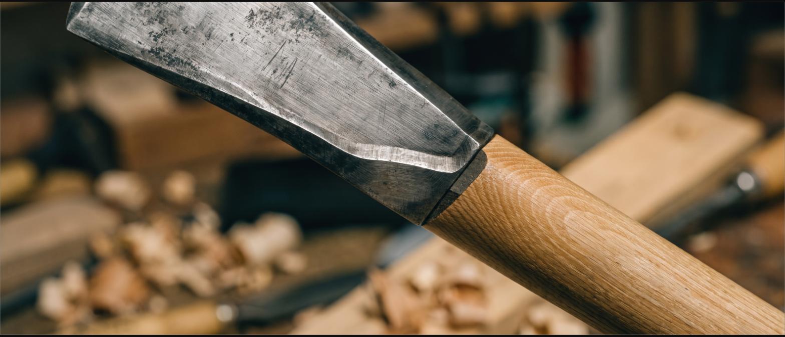Close view of a forged axe head fitted to a hickory handle showing the wedge